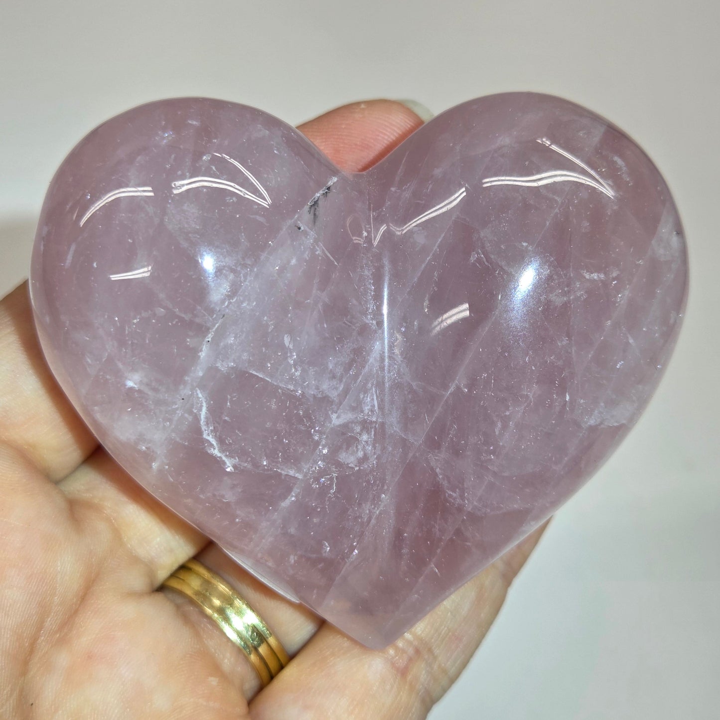 A hand holding a polished heart-shaped rose quartz crystal wand against a plain light background.