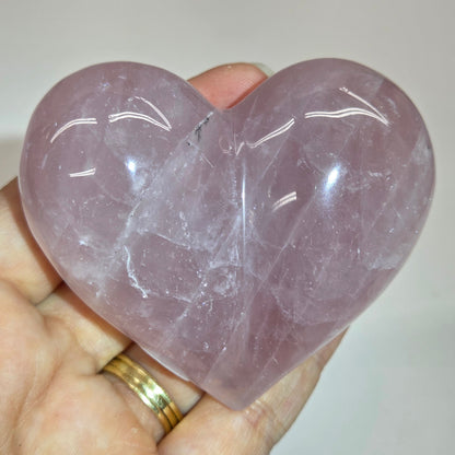 A hand holding a polished heart-shaped rose quartz crystal wand against a plain light background.
