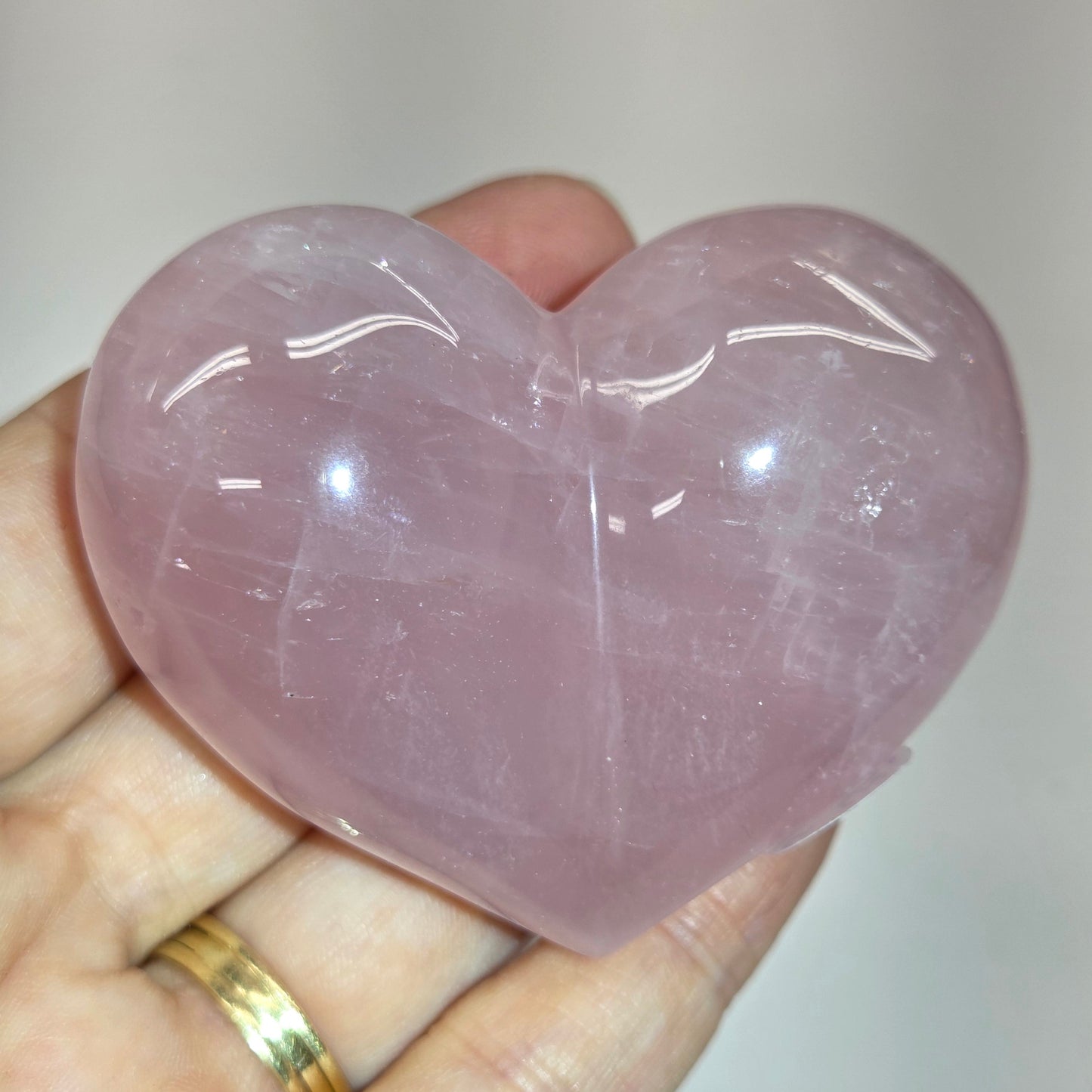 A heart-shaped rose quartz crystal ball held in a person's hand, showing its soft pink color and smooth, polished texture.
