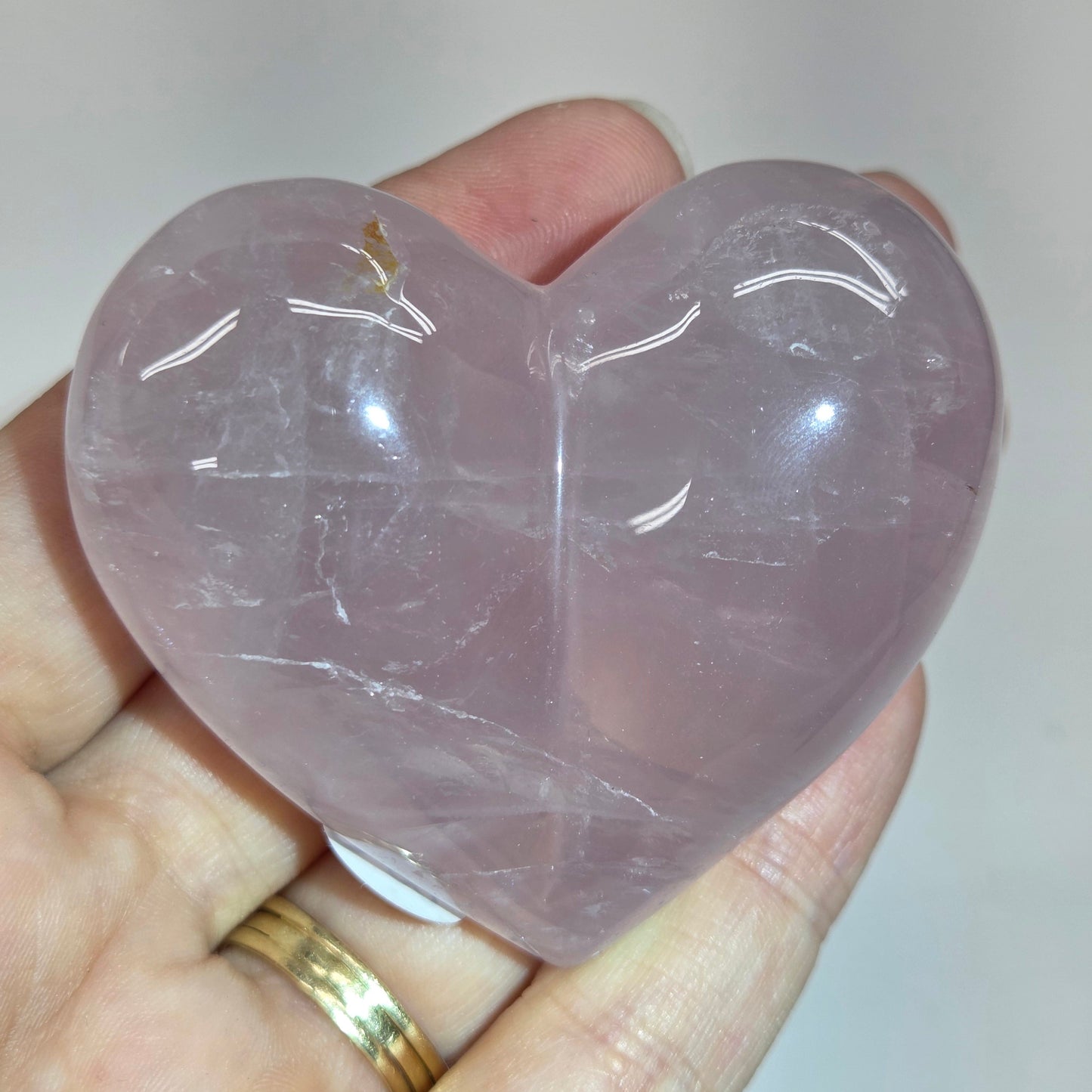 A hand holding a polished, heart-shaped pink quartz crystal against a plain light background.
