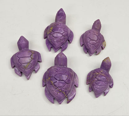 Five small carved turtle figurines in a purple stone with natural gold veining, arranged on a plain off-white background.