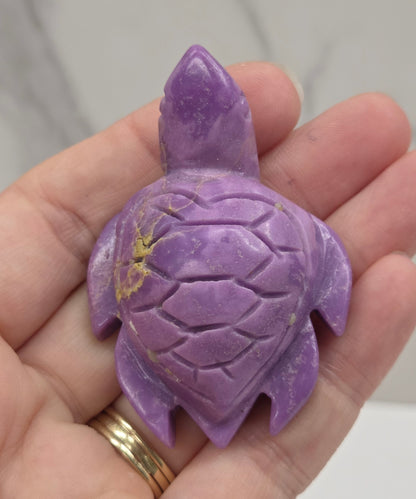 A carved purple turtle figurine held in a person's hand against a light marble-like background.
