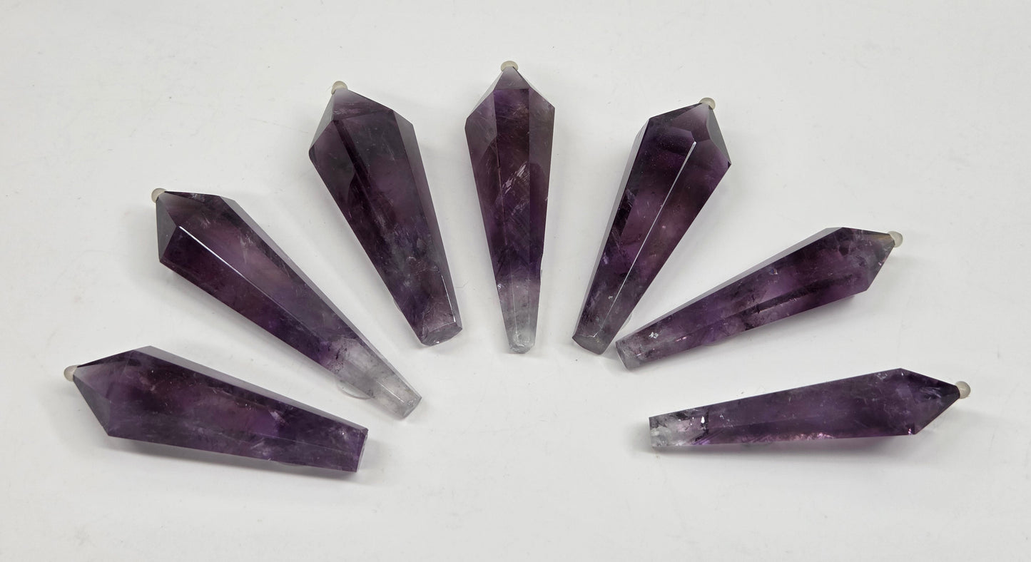 Seven faceted amethyst crystal point pendants arranged in a fan shape on a plain white background.