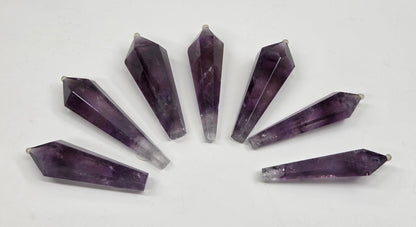 Seven faceted amethyst crystal point pendants arranged in a fan shape on a plain white background.