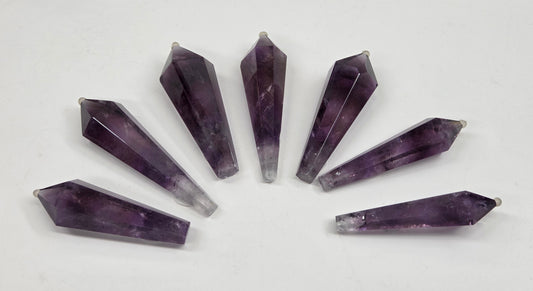 Seven faceted amethyst crystal point pendants arranged in a fan shape on a plain white background.