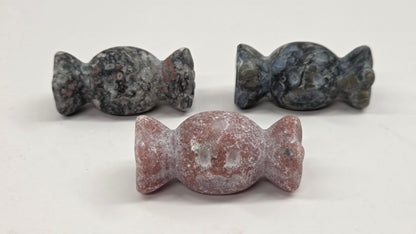 Three small carved stone candy-shaped ornaments displayed on a plain light background, with one in the foreground and two behind it.