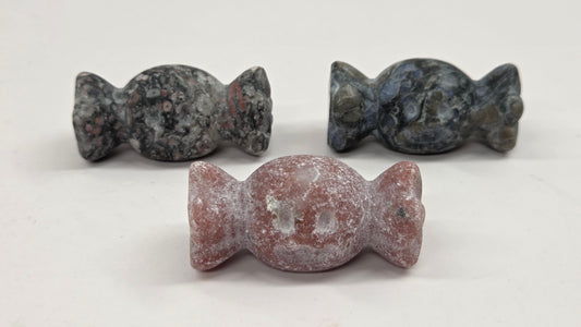Three small carved stone candy-shaped ornaments displayed on a plain light background, with one in the foreground and two behind it.