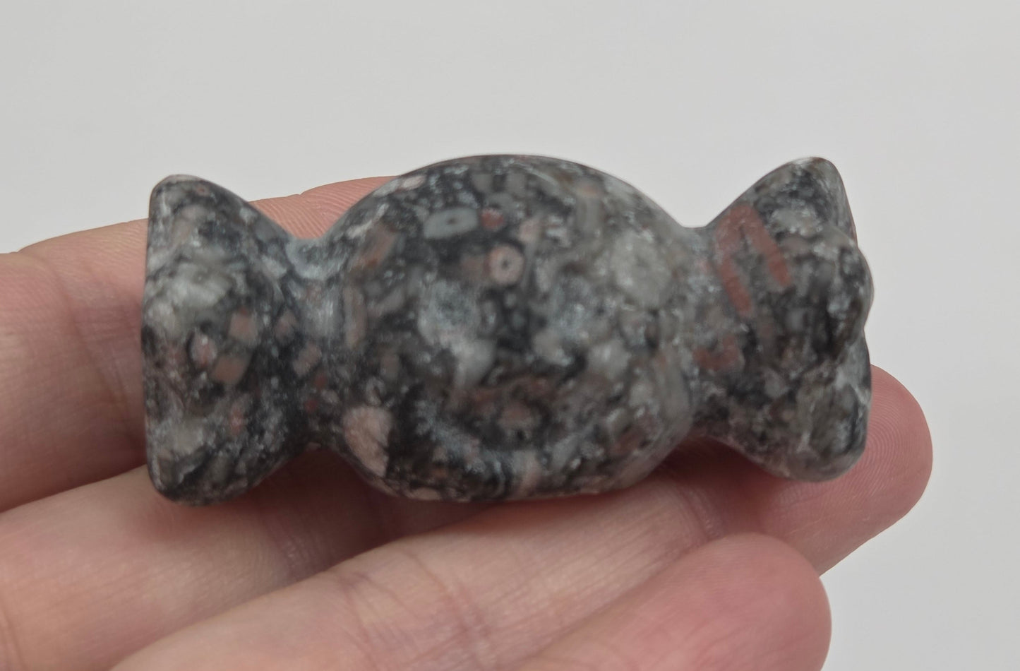 A small carved stone figurine, shaped like a stylized figure with a textured mottled gray, black, and white appearance, held in a person's hand.