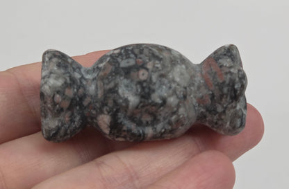 A small carved stone figurine, shaped like a stylized figure with a textured mottled gray, black, and white appearance, held in a person's hand.