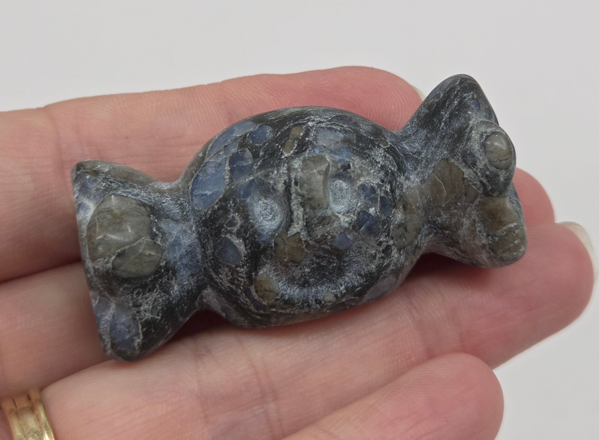 A small carved stone figurine of a frog or toad, held in a person's hand. The figurine is made of a mottled gray and green stone with natural crystalline patterns.