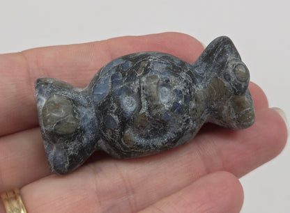 A small carved stone figurine of a frog or toad, held in a person's hand. The figurine is made of a mottled gray and green stone with natural crystalline patterns.
