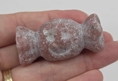 A small carved stone figurine, likely a bird or animal, held in a person's hand. The figurine has a rough, textured surface with light gray and reddish-brown tones.