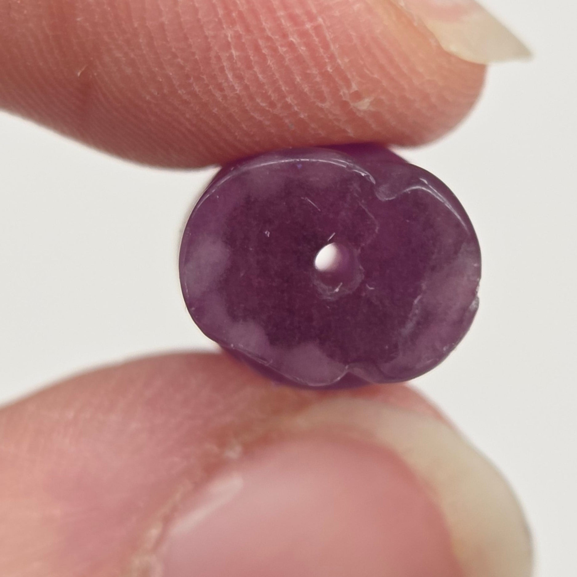 A small, round, polished purple gemstone bead held between two fingers against a plain light background.