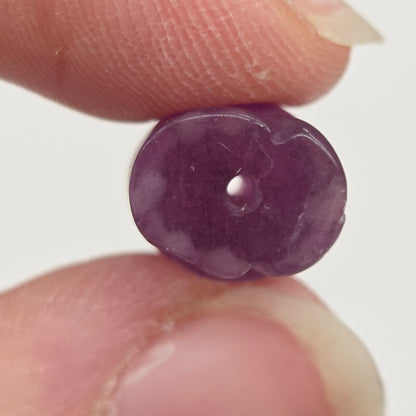 A small, round, polished purple gemstone bead held between two fingers against a plain light background.
