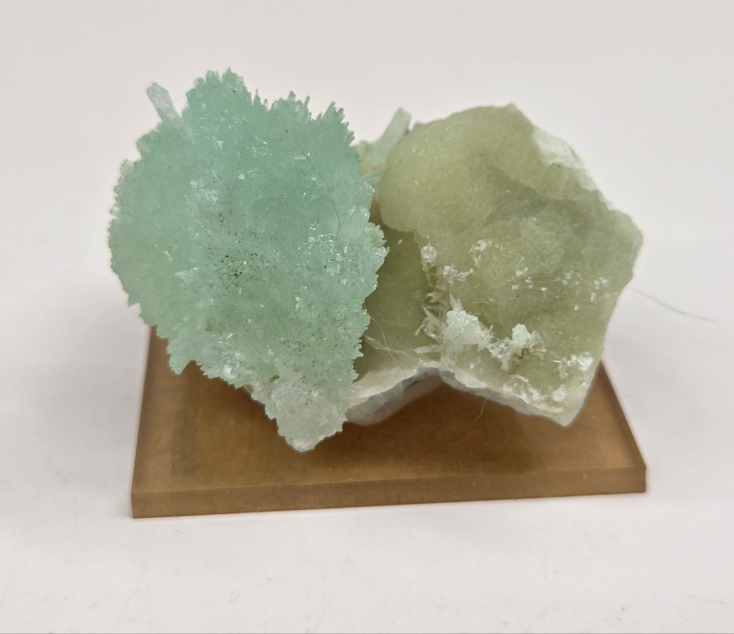 A natural mineral specimen featuring light green and pale gray crystalline formations mounted on a square brown wooden display base, photographed against a plain white background.