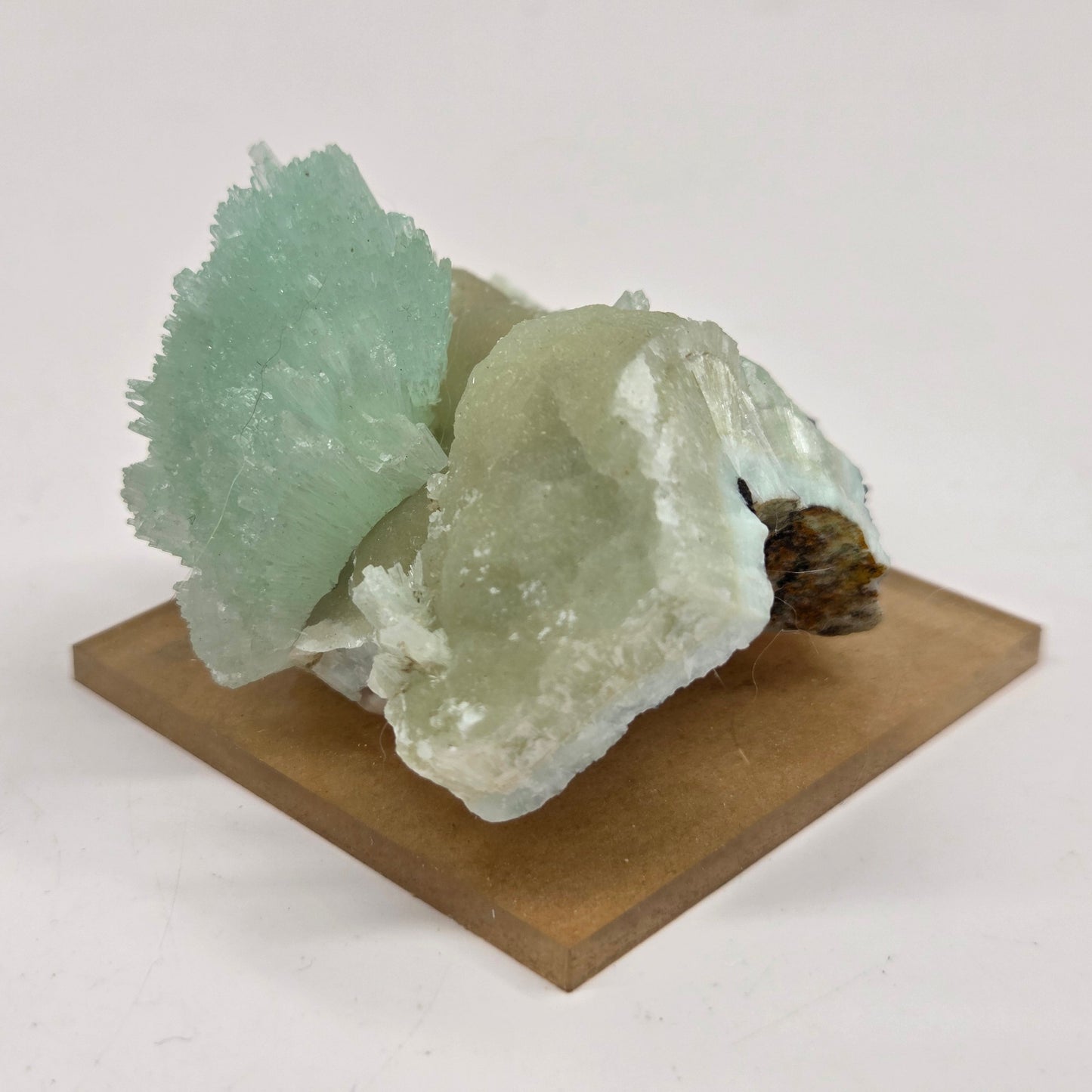 A pale green and milky white crystal cluster mounted on a square tan display block, photographed against a plain light background.