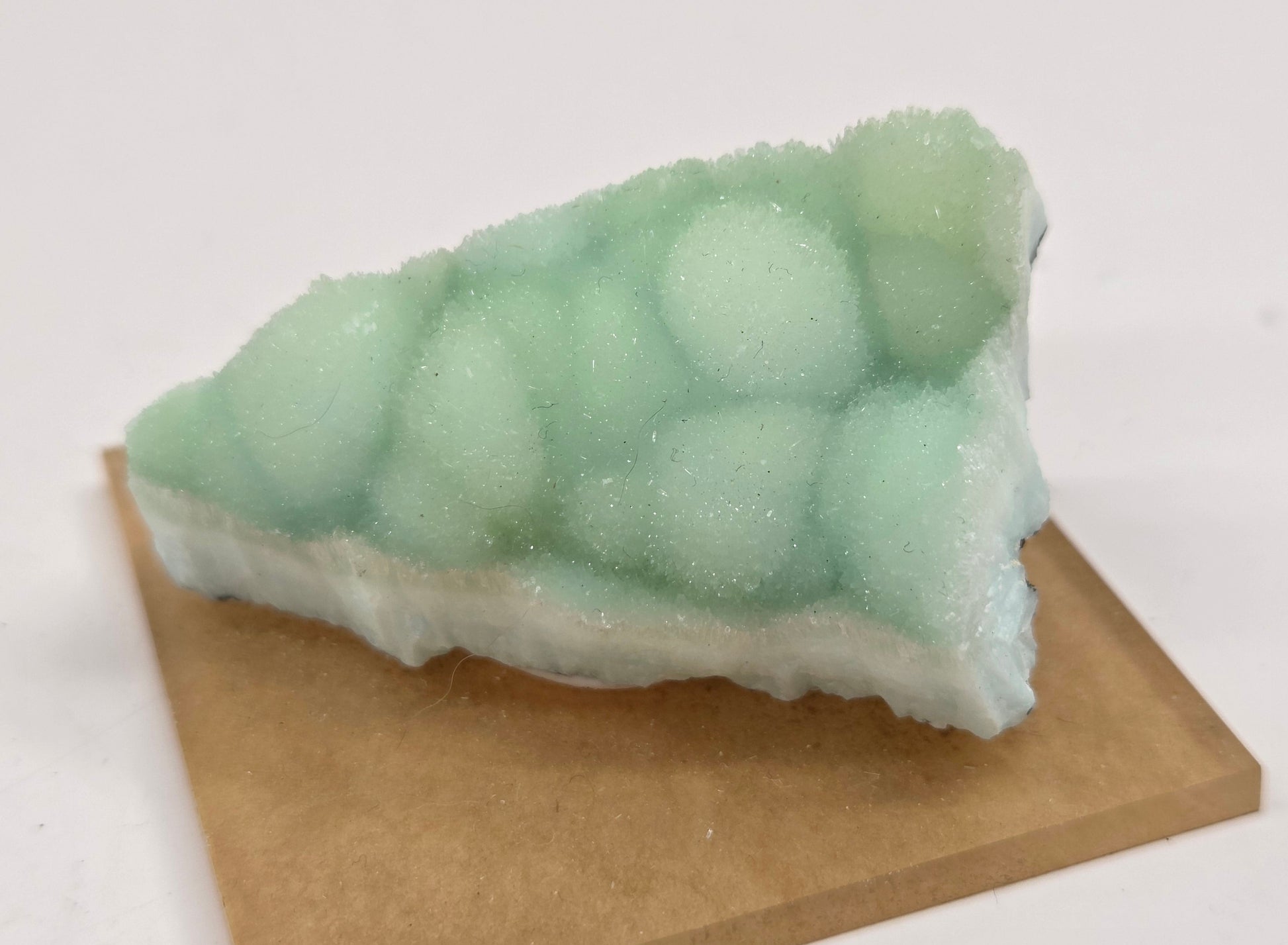 A triangular wedge-shaped product with a frosted mint green top and white base, displayed on a brown rectangular block against a plain white background.