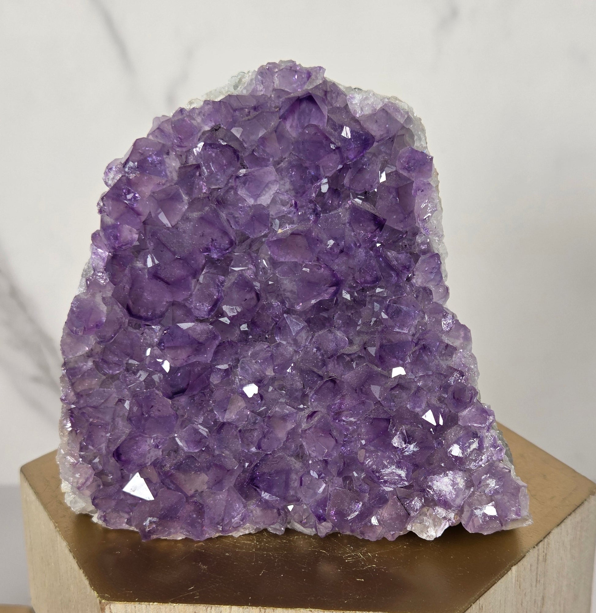 A purple amethyst crystal cluster mounted on a light wood block, photographed against a white marble-patterned background.