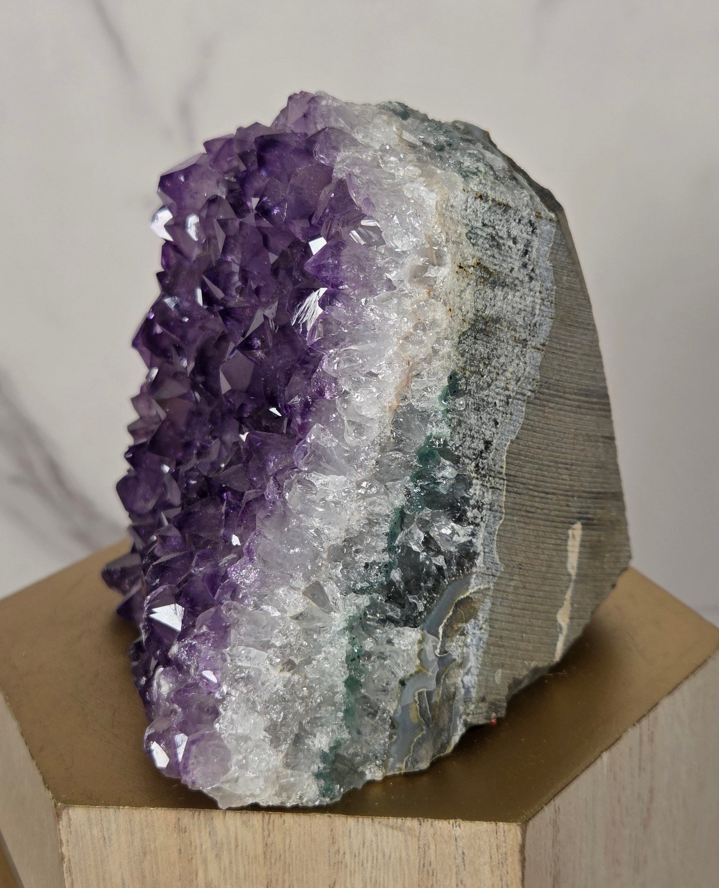 A natural amethyst crystal cluster geode mount displayed on a light wood geometric block against a white marble background.