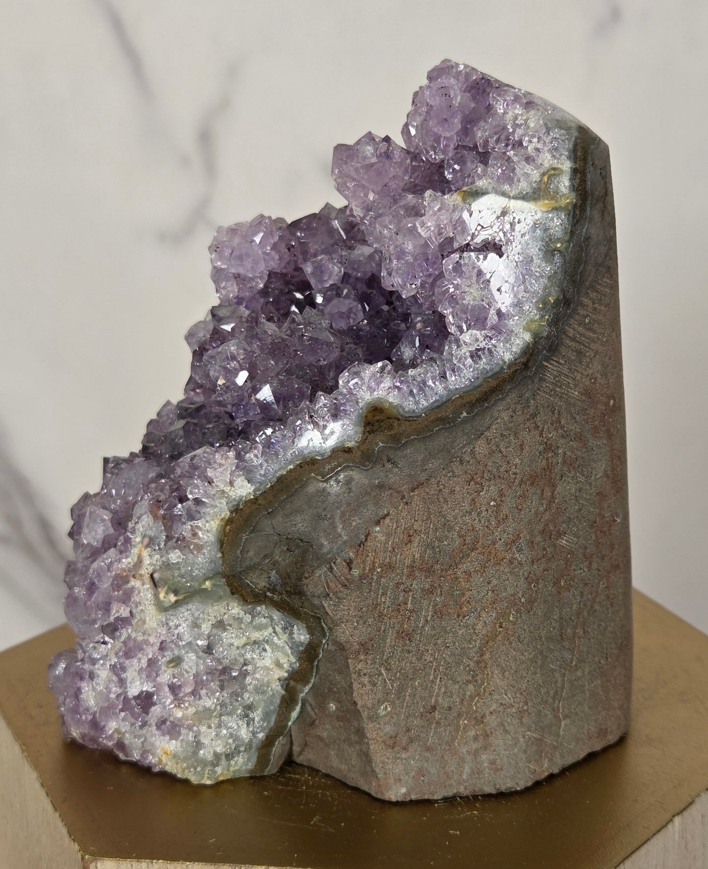 A raw amethyst geode specimen mounted on a wooden display block, showing a purple crystal cluster against a gray-brown matrix.