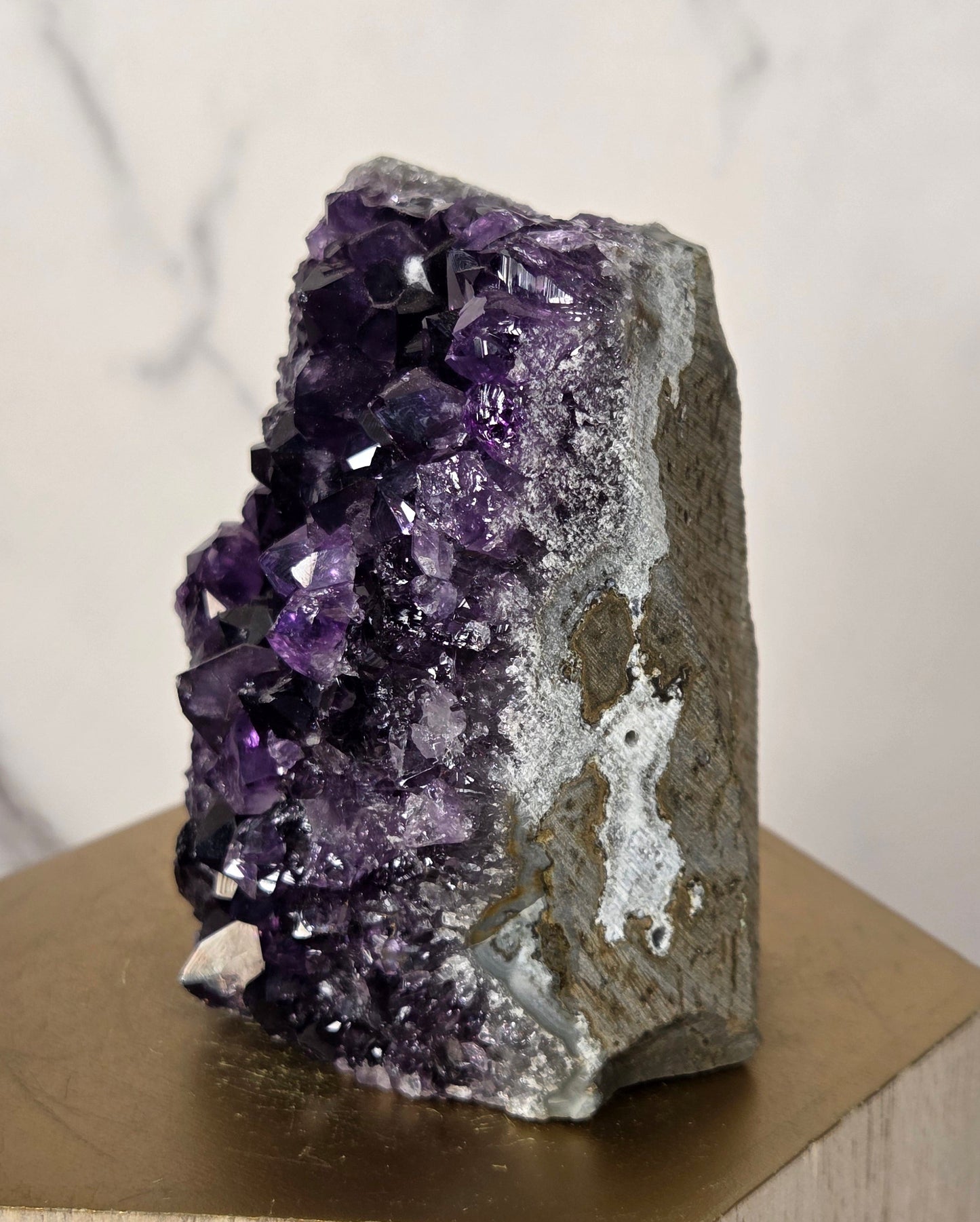 A raw amethyst crystal cluster with deep purple and white crystalline formations, mounted on a light wood geometric display stand against a white marble background.