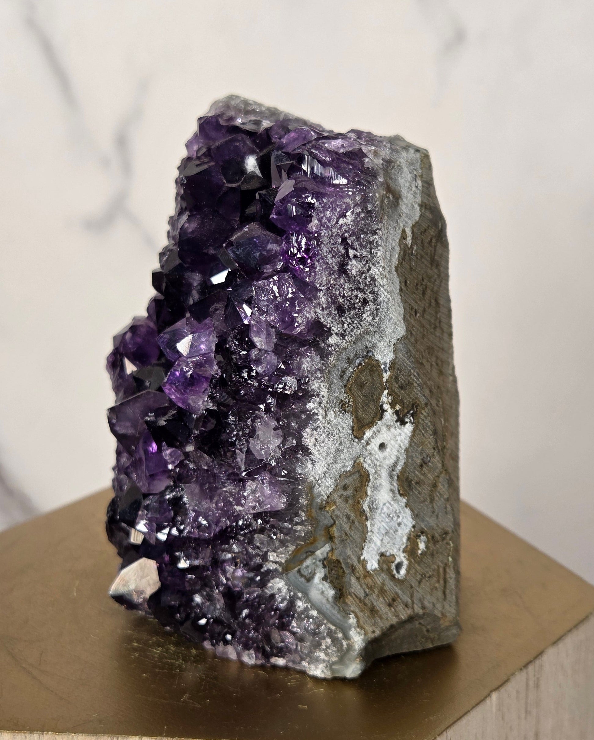 A raw amethyst crystal cluster with deep purple and white crystalline formations, mounted on a light wood geometric display stand against a white marble background.
