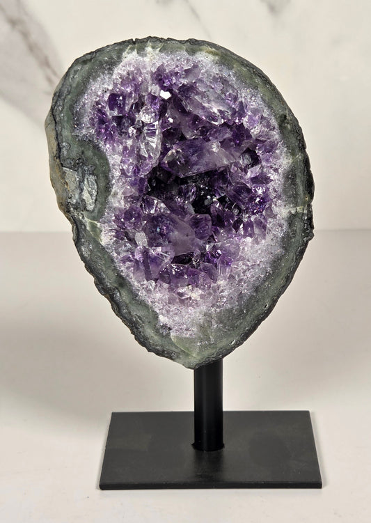 Amethyst geode on a metal stand against a white background