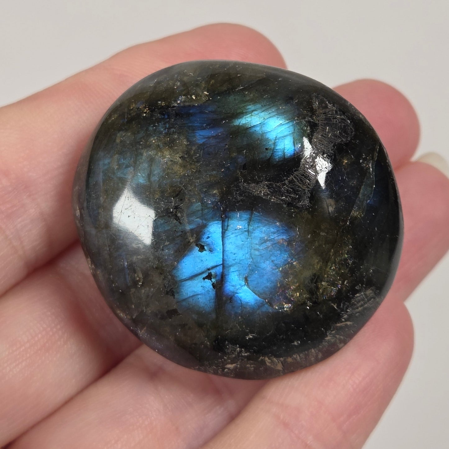 A polished labradorite gemstone with a blue flash, held in a person's hand against a plain light background.