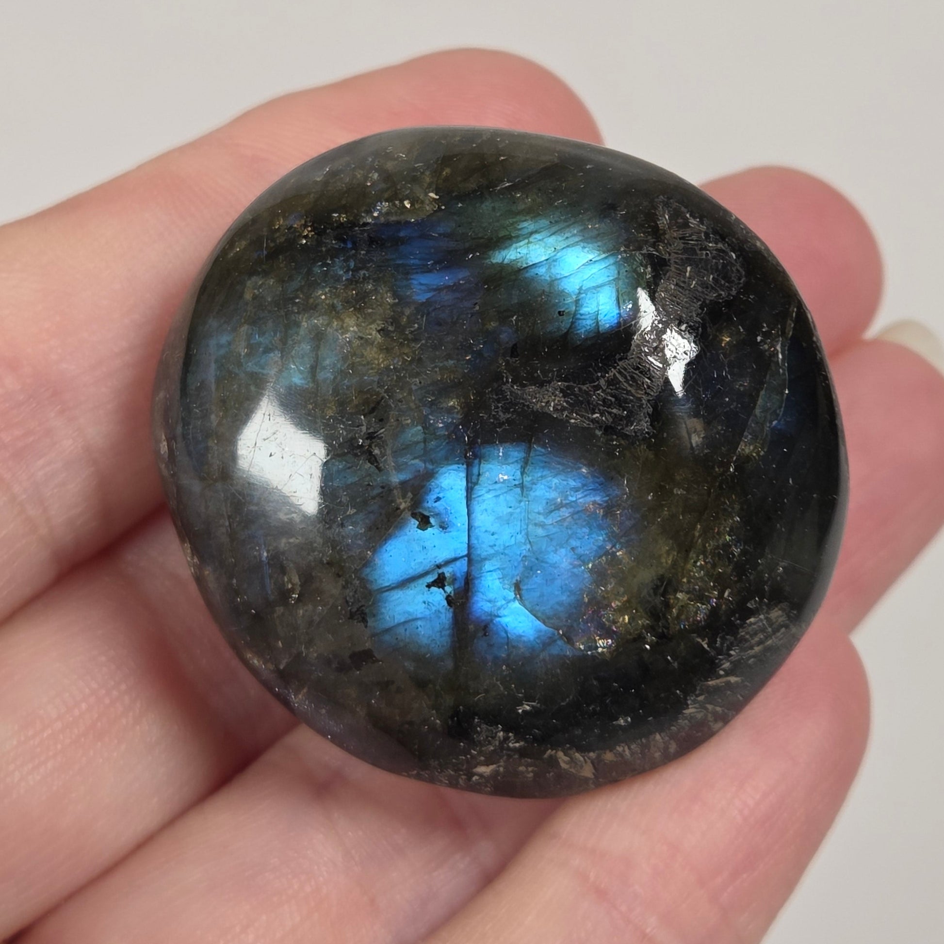 A polished labradorite gemstone with a blue flash, held in a person's hand against a plain light background.