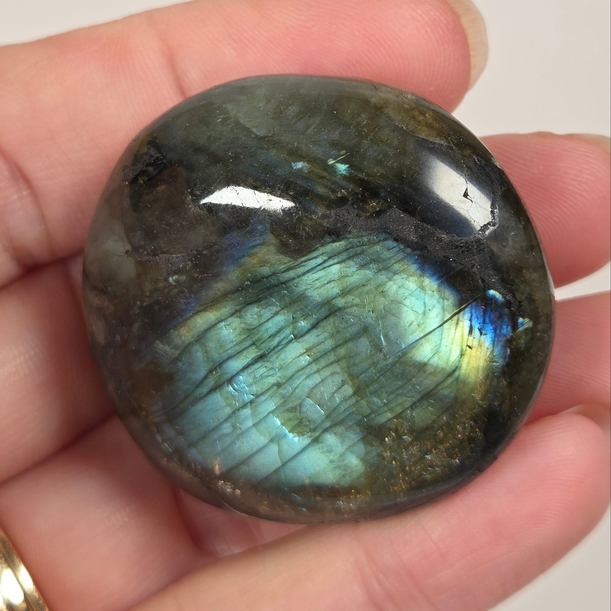 A polished round labradorite gemstone with a shimmering blue-green iridescent flash, held in a person's hand against a plain light background.