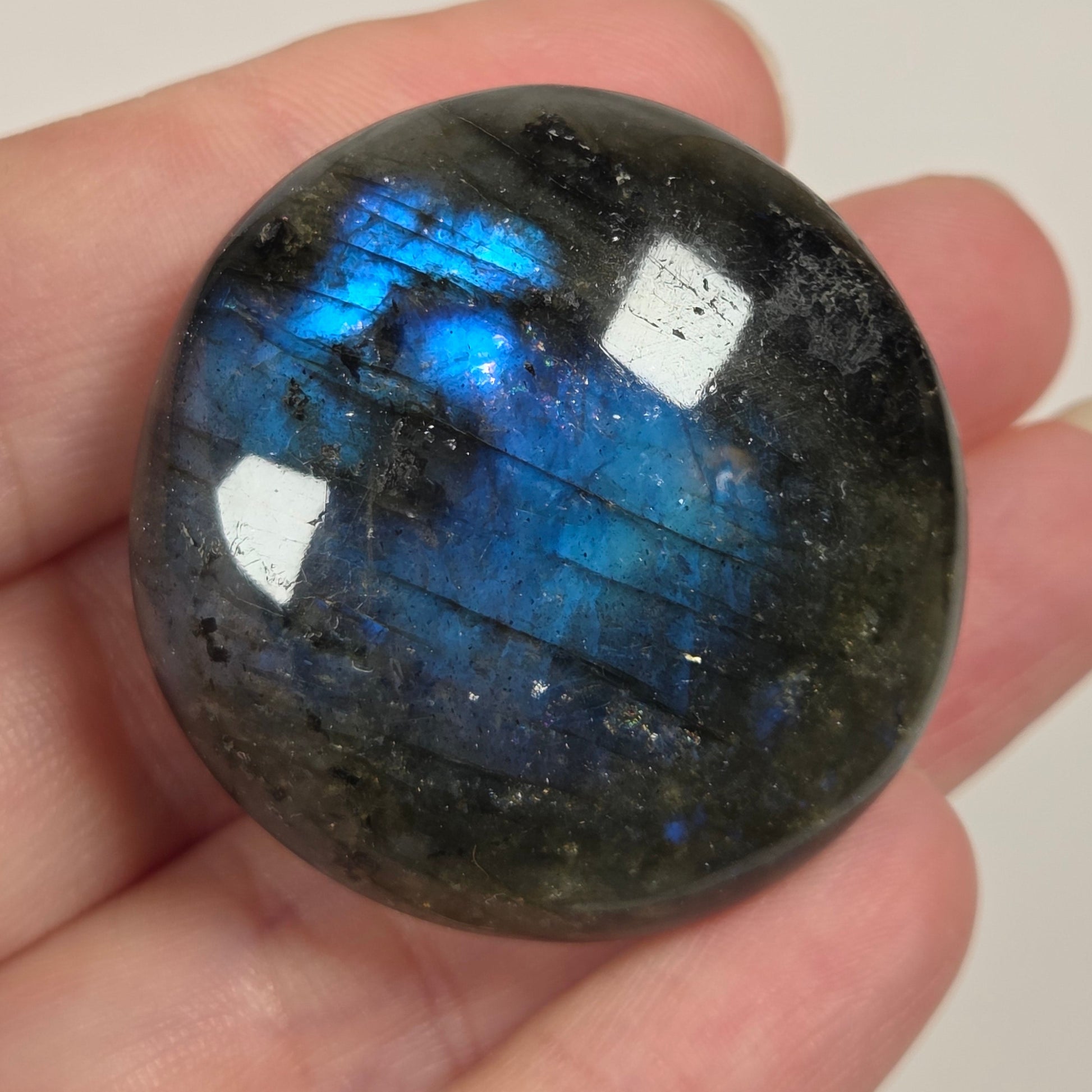 A polished labradorite gemstone with vibrant blue and white flash, held in a person's hand against a plain light background.