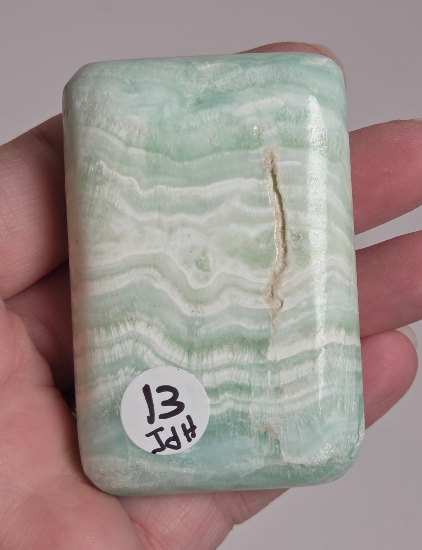 Banded calcite crystal carved into the shape of a soap bar with blue, green and brown coloring being held in a hand on a white background