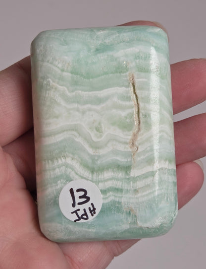 Banded calcite crystal carved into the shape of a soap bar with blue, green and brown coloring being held in a hand on a white background