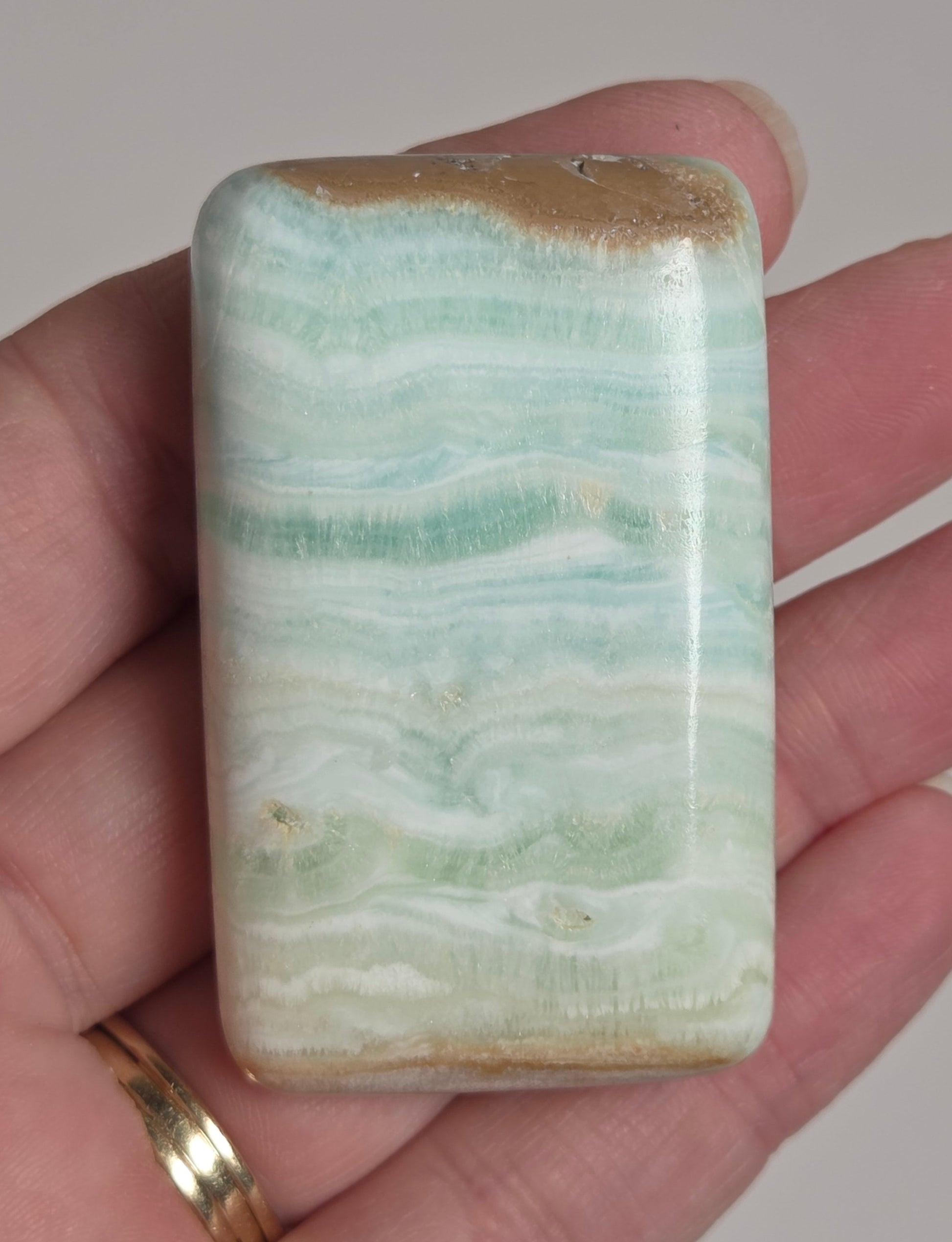 Banded calcite crystal carved into the shape of a soap bar with blue, green and brown coloring being held in a hand on a white background