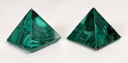 Hand holding a Green malachite crystal carved into the shape of a pyramide against a white background