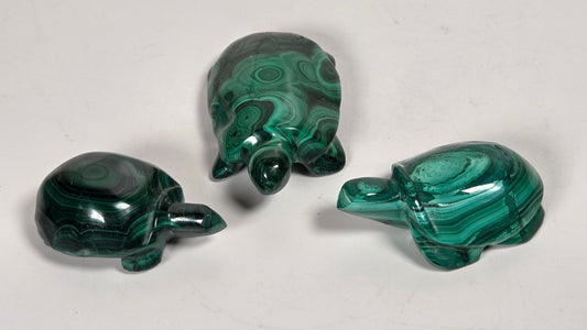 Green malachite crystal carved into the shape of turtles against a white background