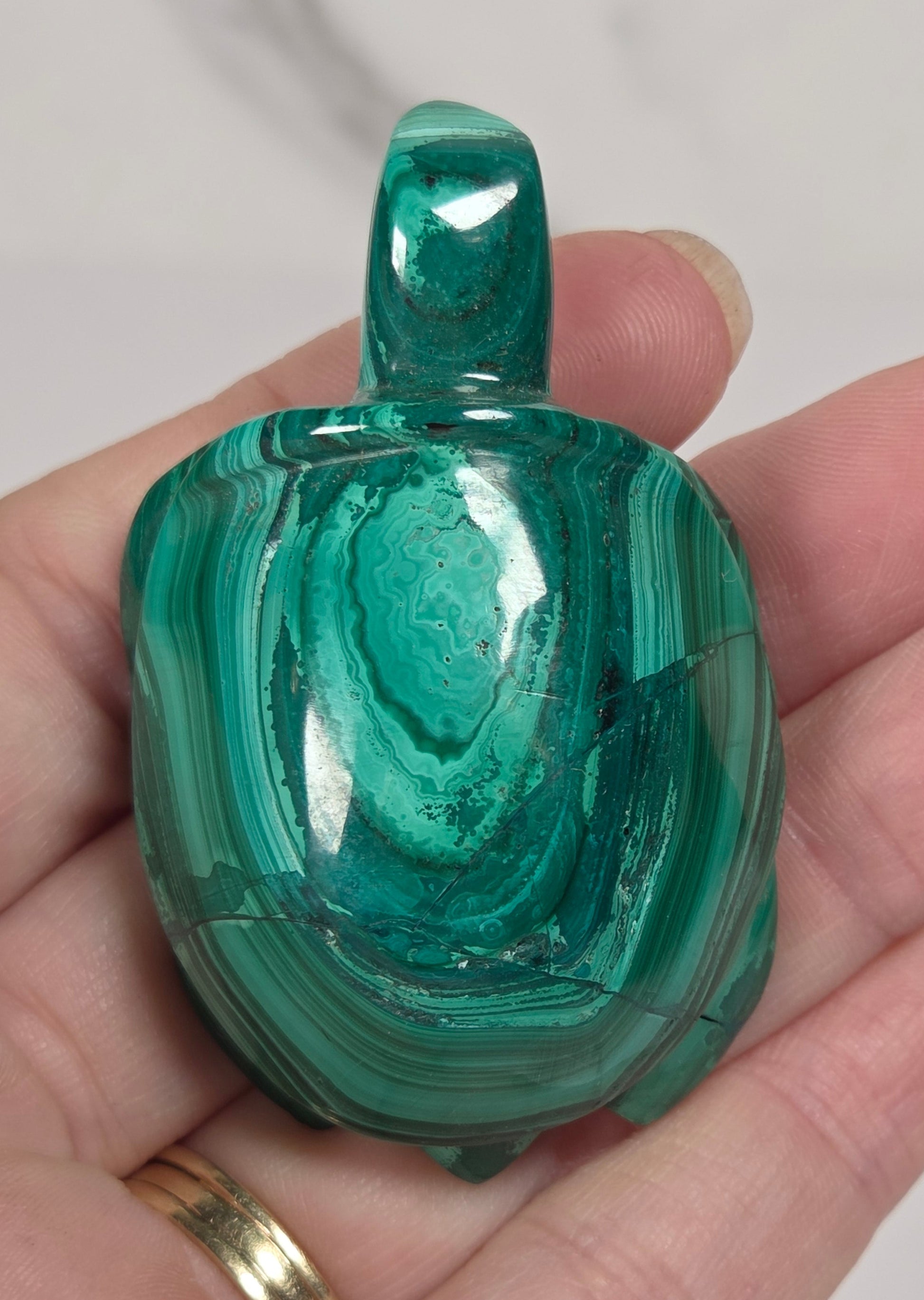 A polished green malachite carved pendant or charm with natural banded patterns, held in a person's hand against a light marble background.
