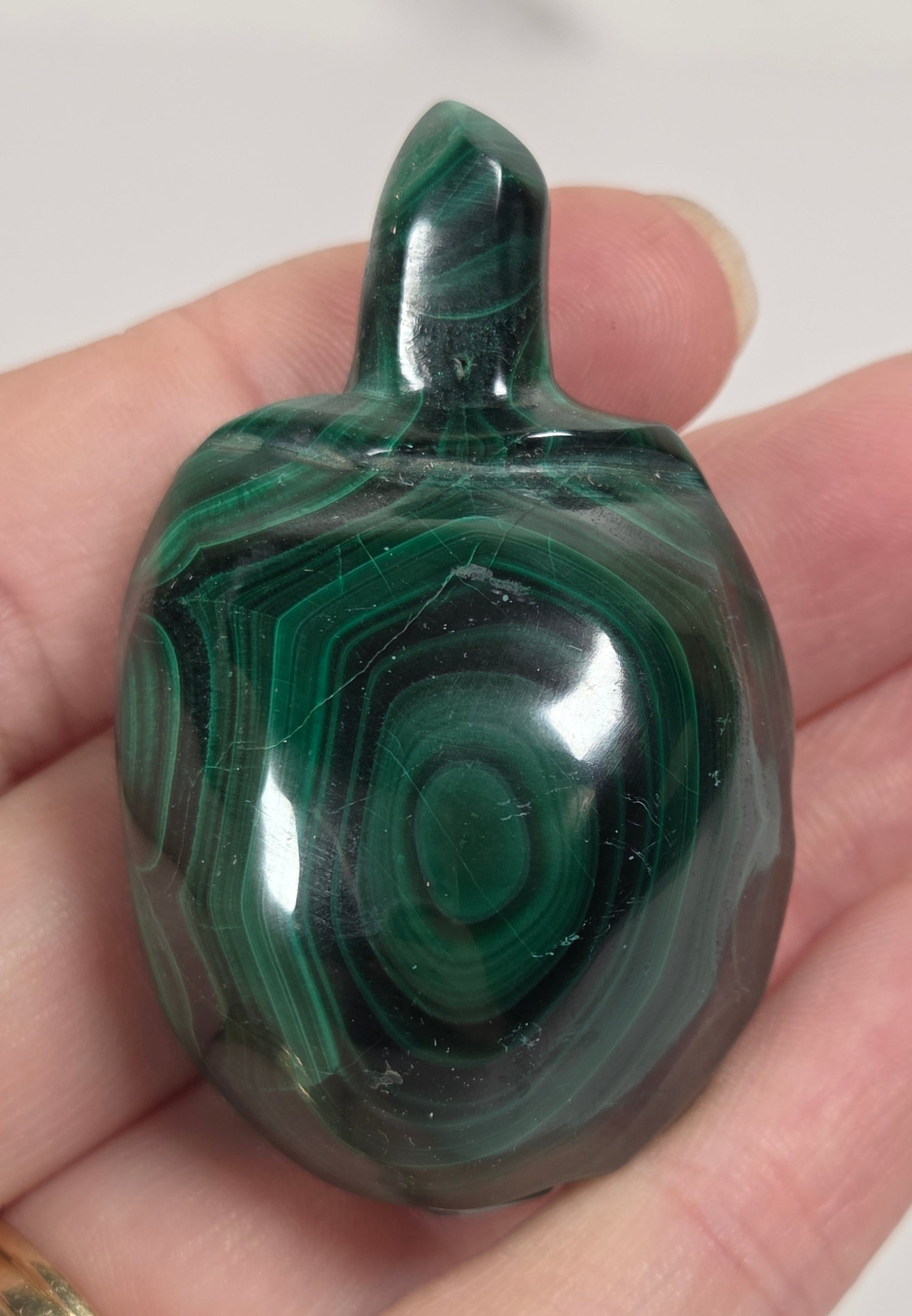 A polished green malachite stone tassel ornament held in a person's hand against a light neutral background.