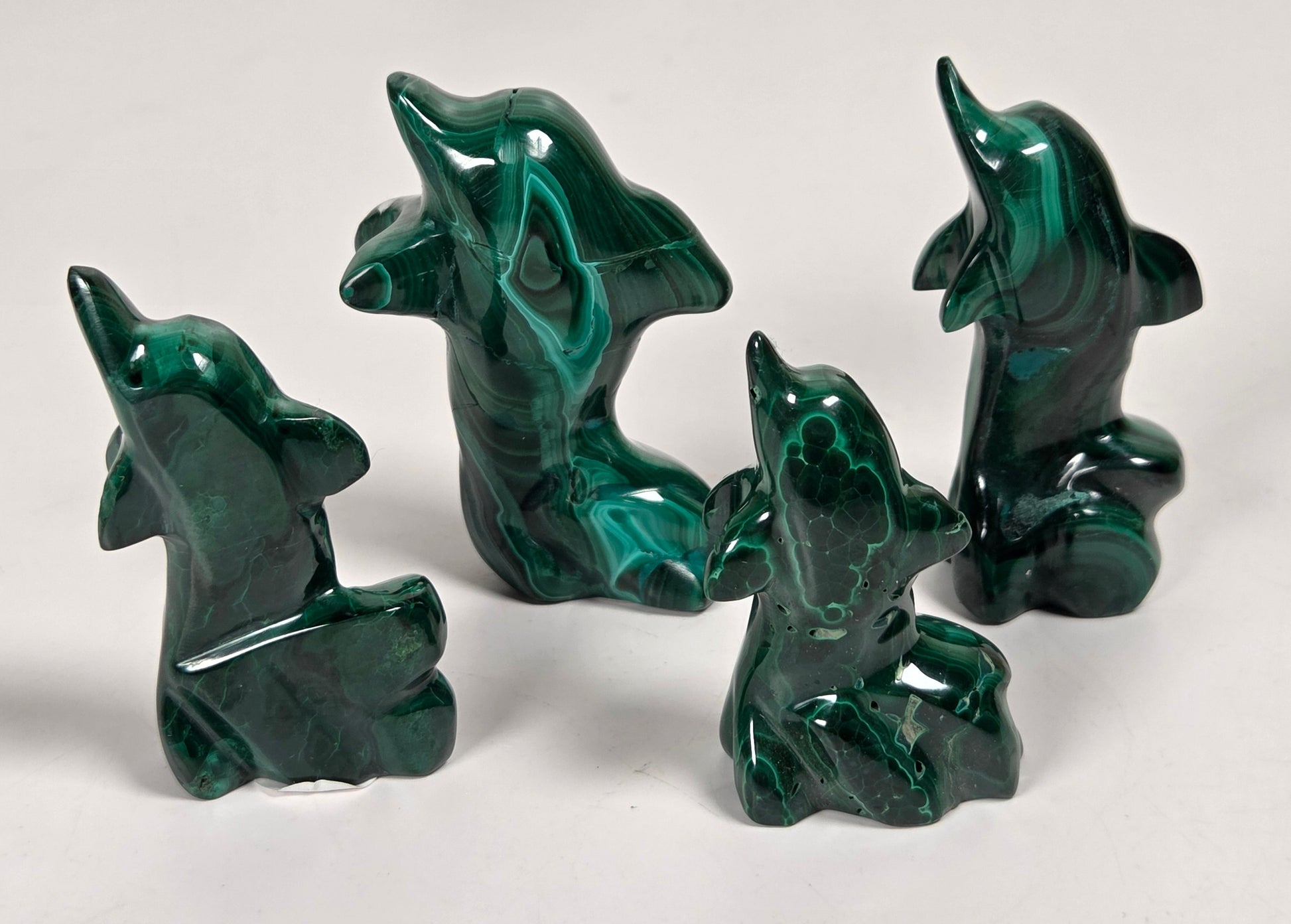 Green malachite crystals carved into the shape of dolphins against a white background