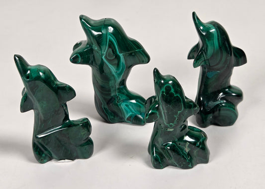 Green malachite crystals carved into the shape of dolphins against a white background
