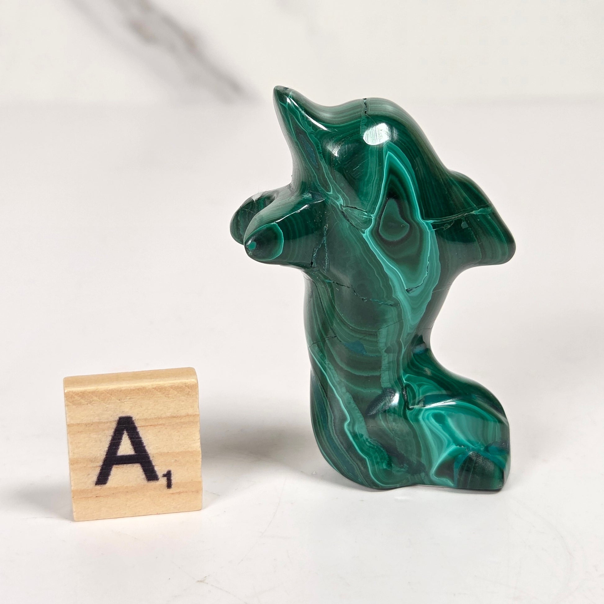 Green malachite crystal carved into the shape of a dolphin against a white background