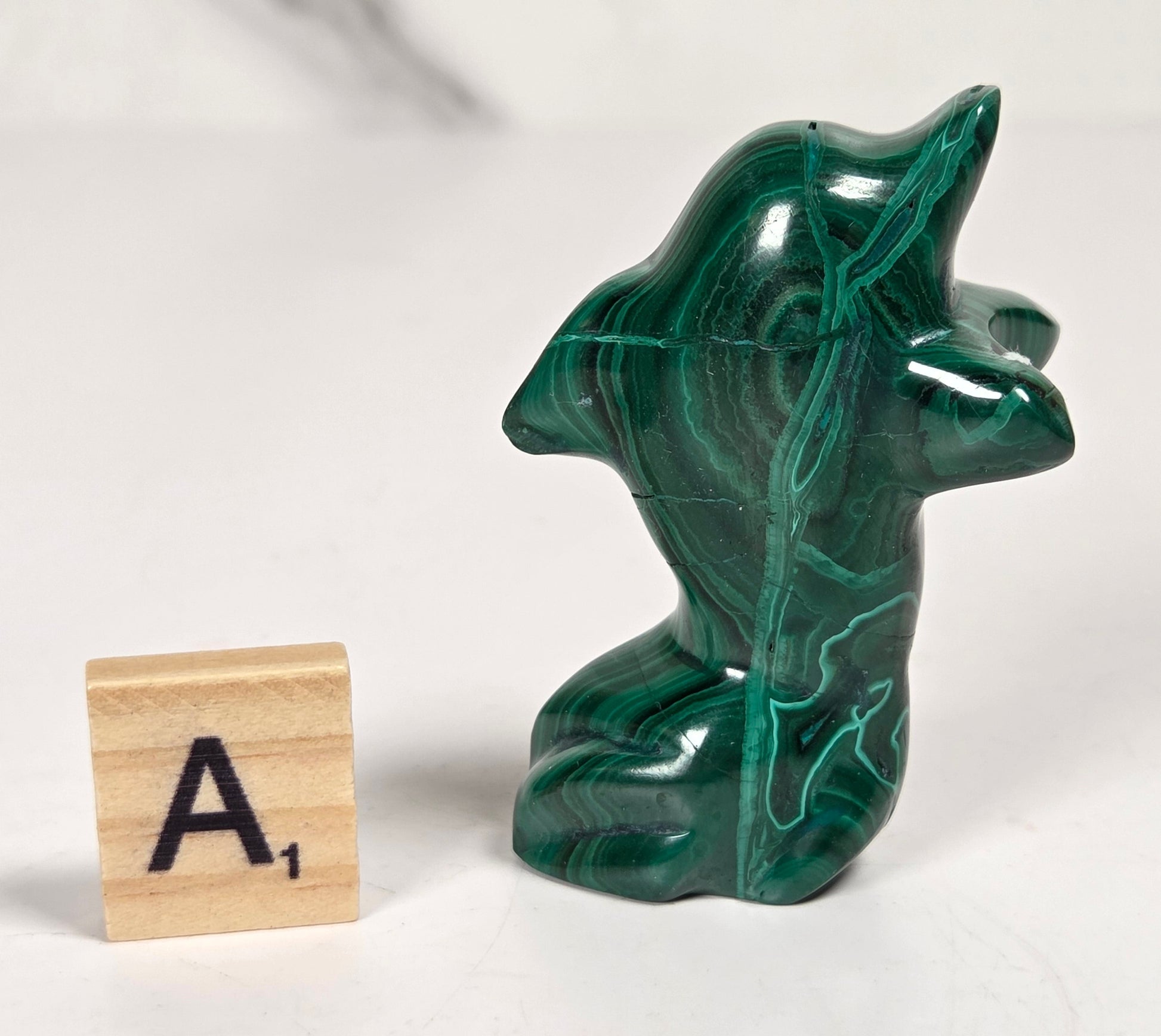 Green malachite crystal carved into the shape of a dolphin against a white background