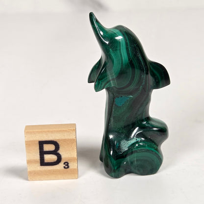 Green malachite crystal carved into the shape of a dolphin against a white background
