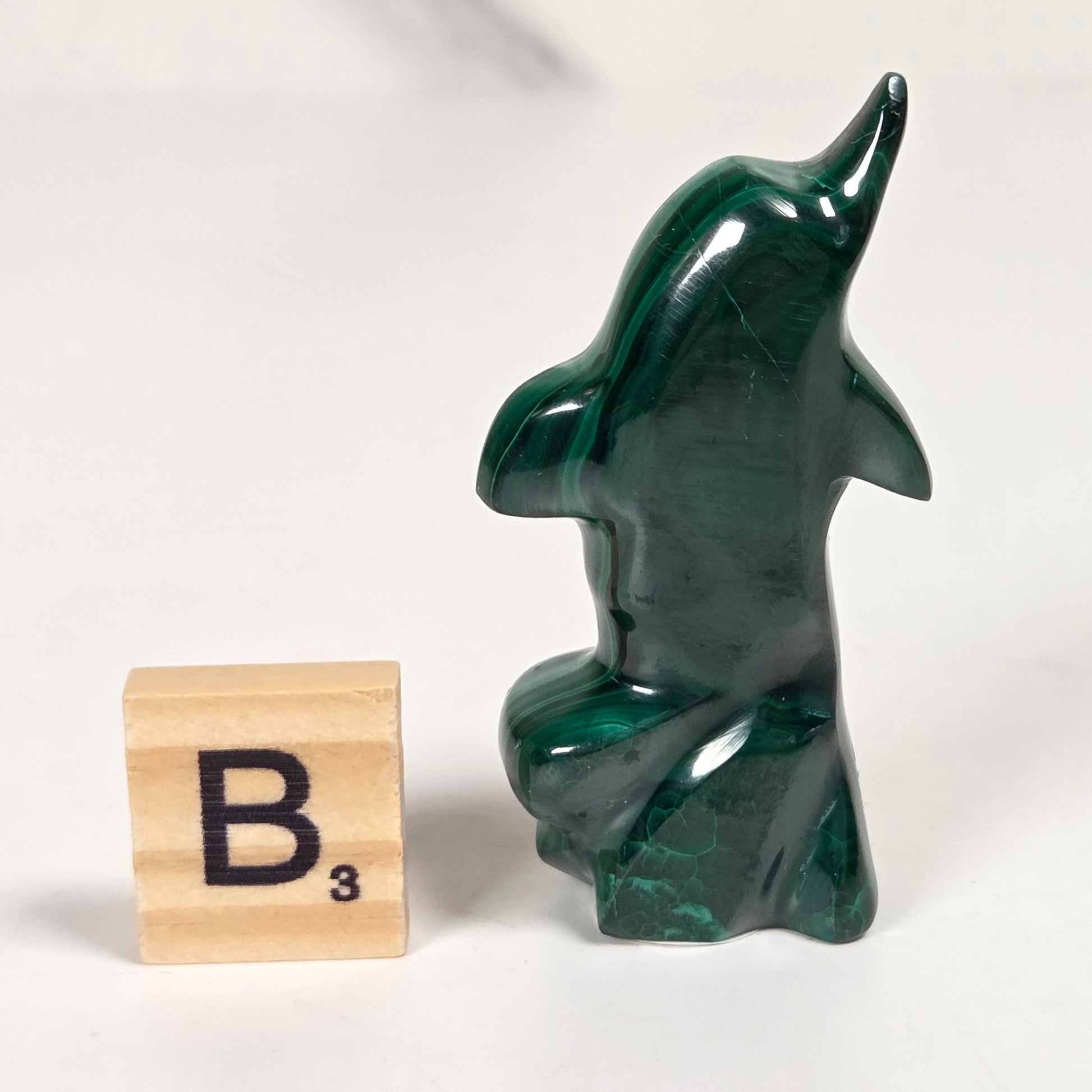 Green malachite crystal carved into the shape of a dolphin against a white background