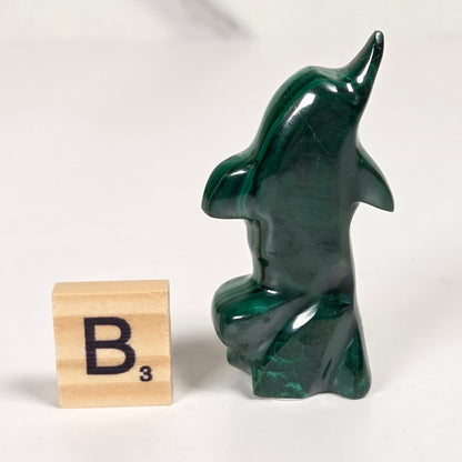 Green malachite crystal carved into the shape of a dolphin against a white background