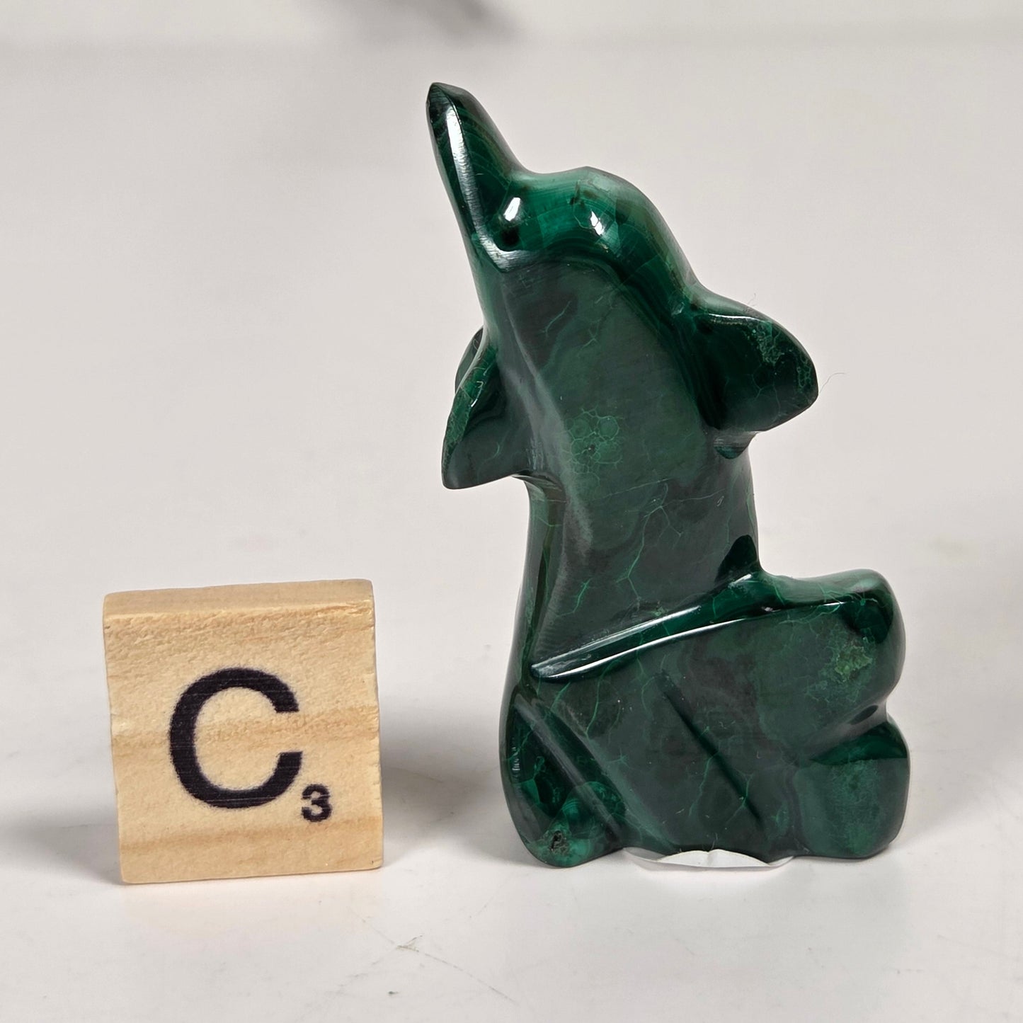 Green malachite crystal carved into the shape of a dolphin against a white background