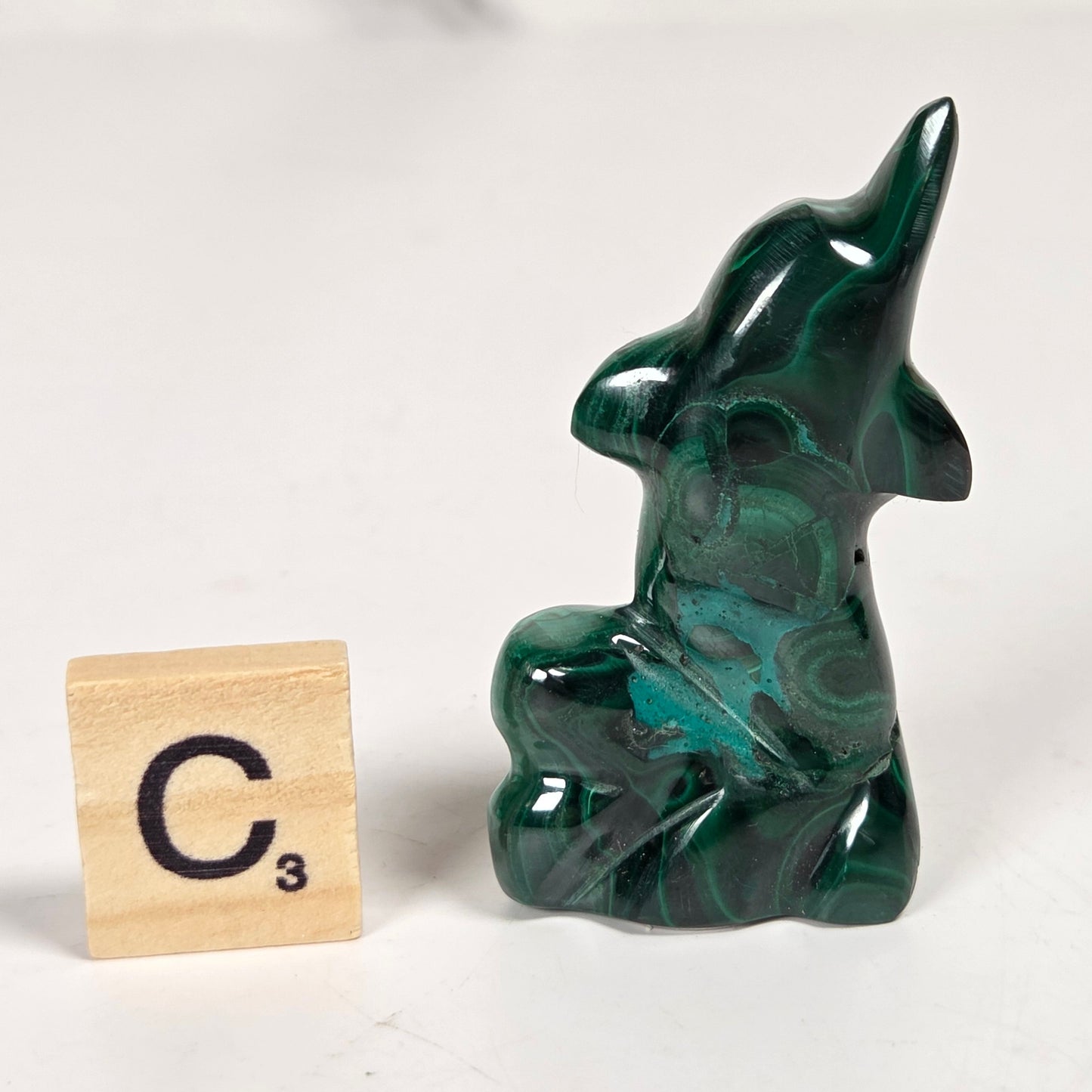 Green malachite crystal carved into the shape of a dolphin against a white background