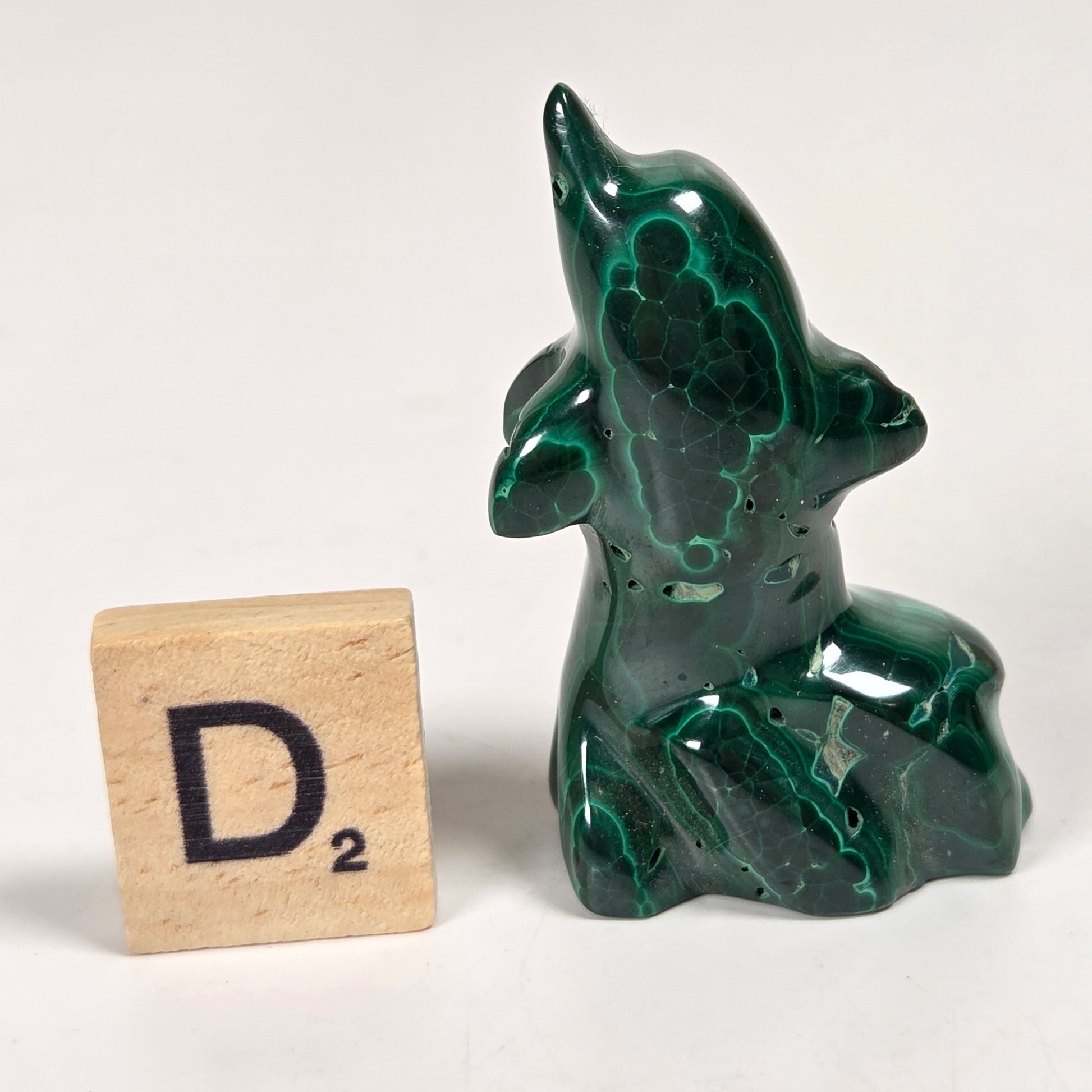 Green malachite crystal carved into the shape of a dolphin against a white background