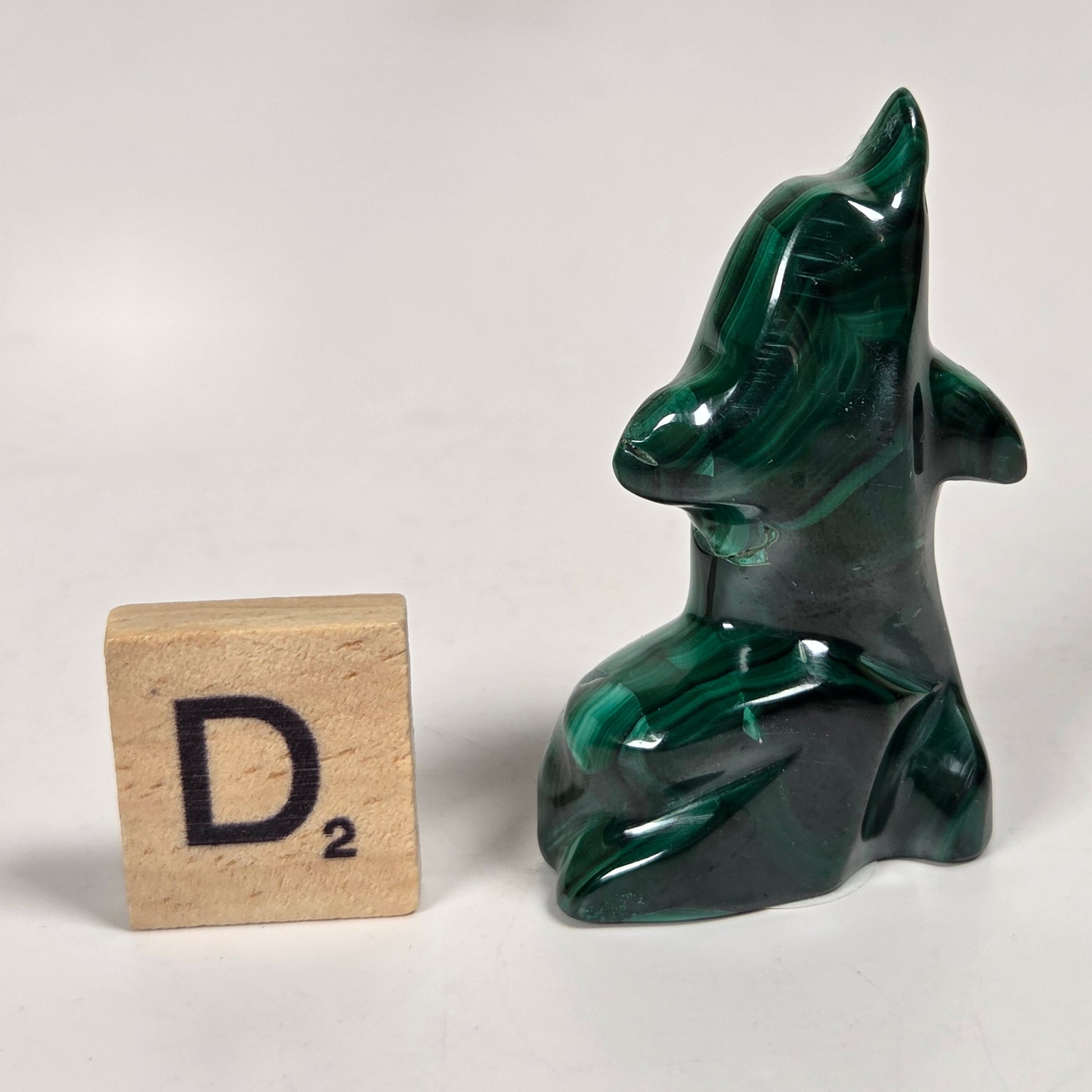 Green malachite crystal carved into the shape of a dolphin against a white background