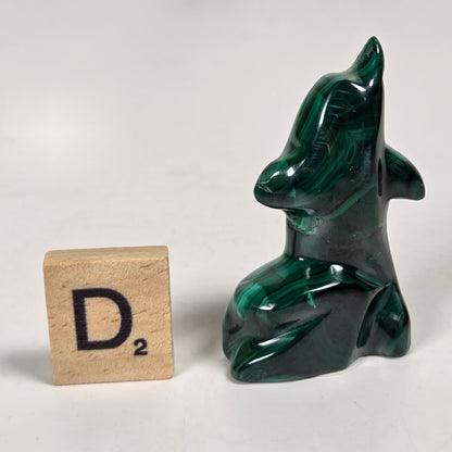 Green malachite crystal carved into the shape of a dolphin against a white background
